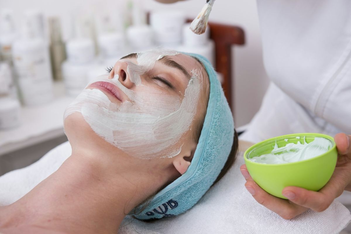 Estetista che applica una maschera bianca sul viso di una cliente